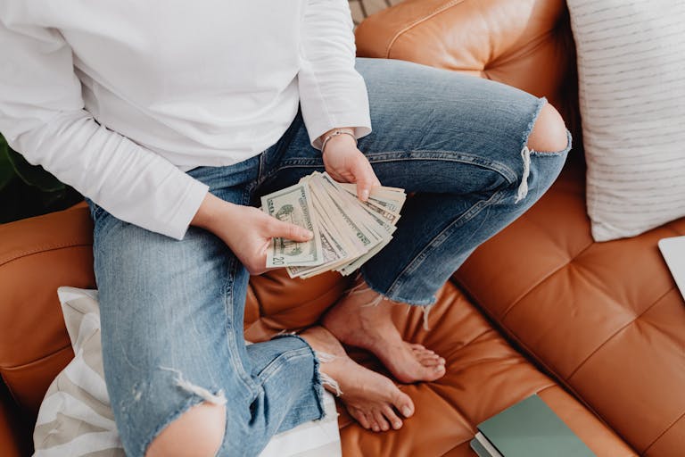 Close-up of a person holding and counting cash while sitting on a leather couch at home.